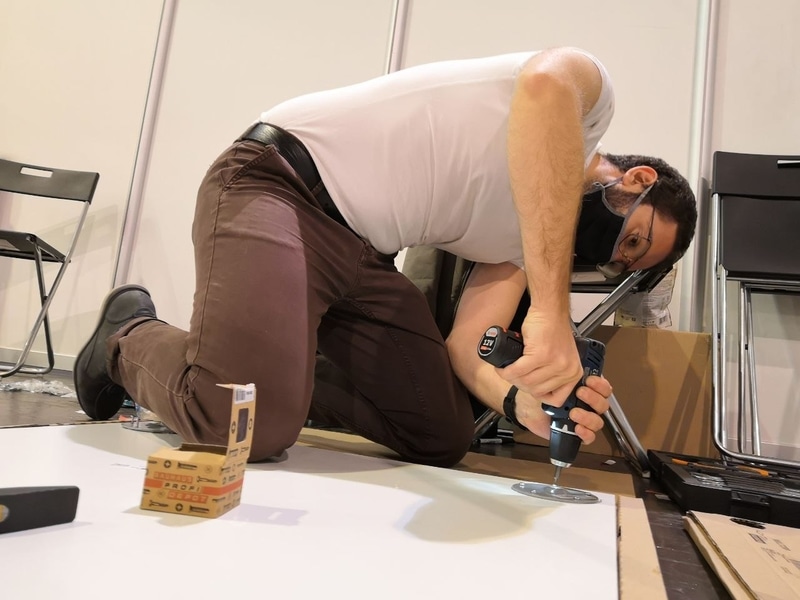 A boy uses an electric screwdiver on a table lying on the floor